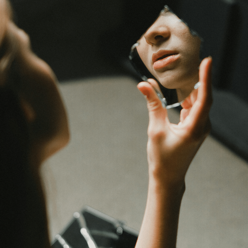 A woman looks into a broken part of a mirror, reflecting back to the viewer.