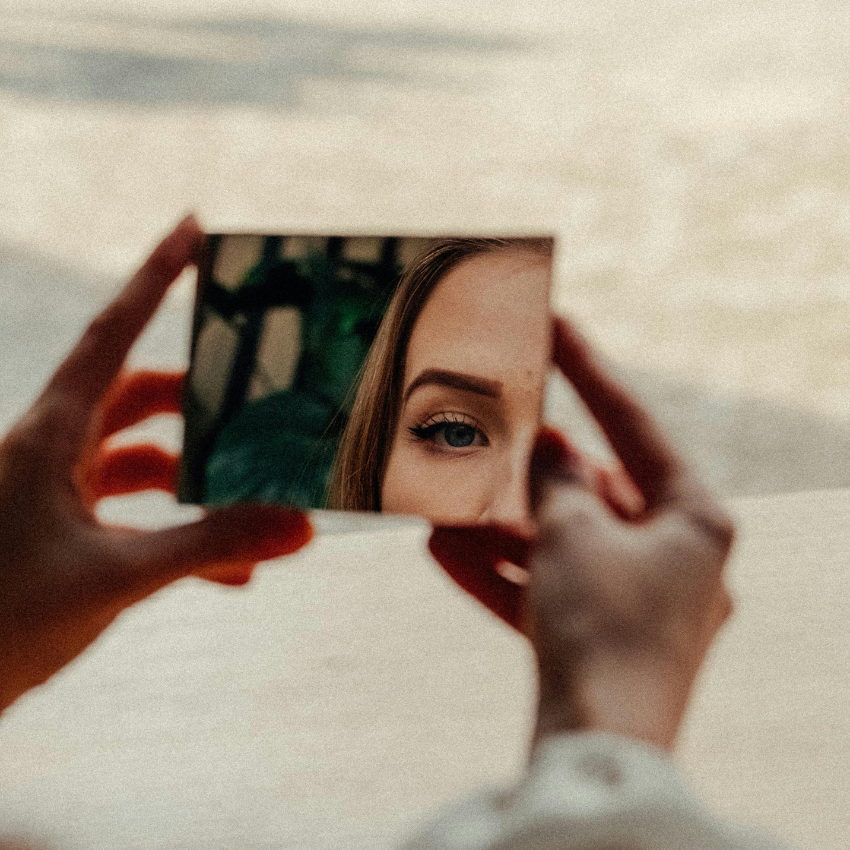 Two hands hold a rectangular mirror with a woman