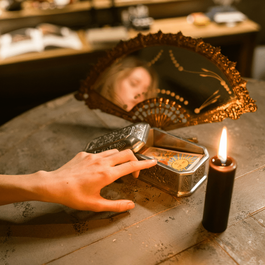 A hand touches a deck of Tarot cards that is next to a lit lighter. A woman