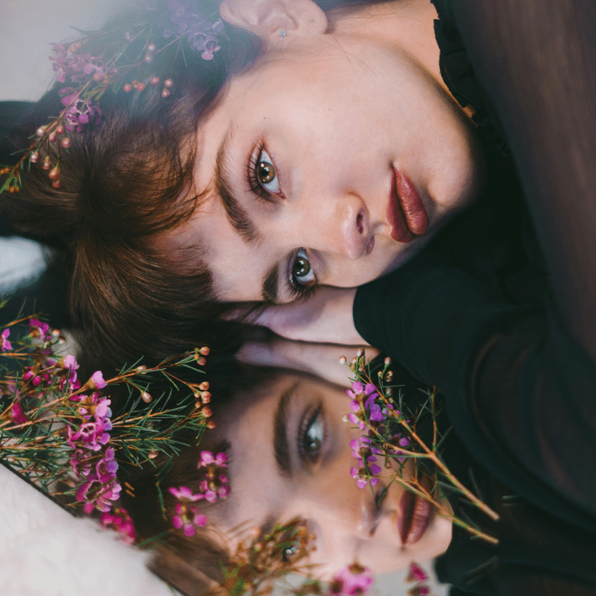 A woman lays down on a mirror, reflecting back her reflection.
