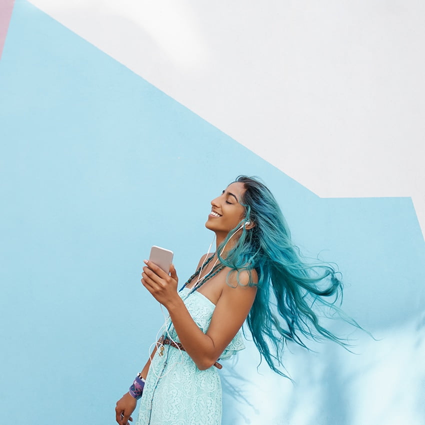 A woman with blue hair is holding her phone, eyes closed, and smiling representing the eccentric energy of Aquarius.