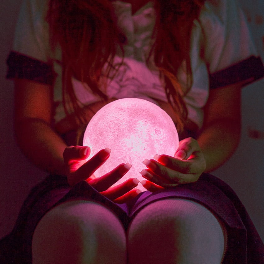 A woman holds a pink orb, representing the Full Moon in Leo.