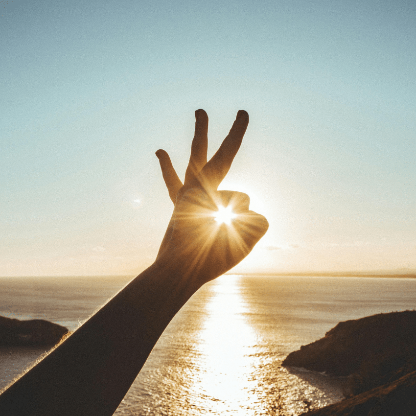 Someone holds their hand up to the sun on the horizon, forming an