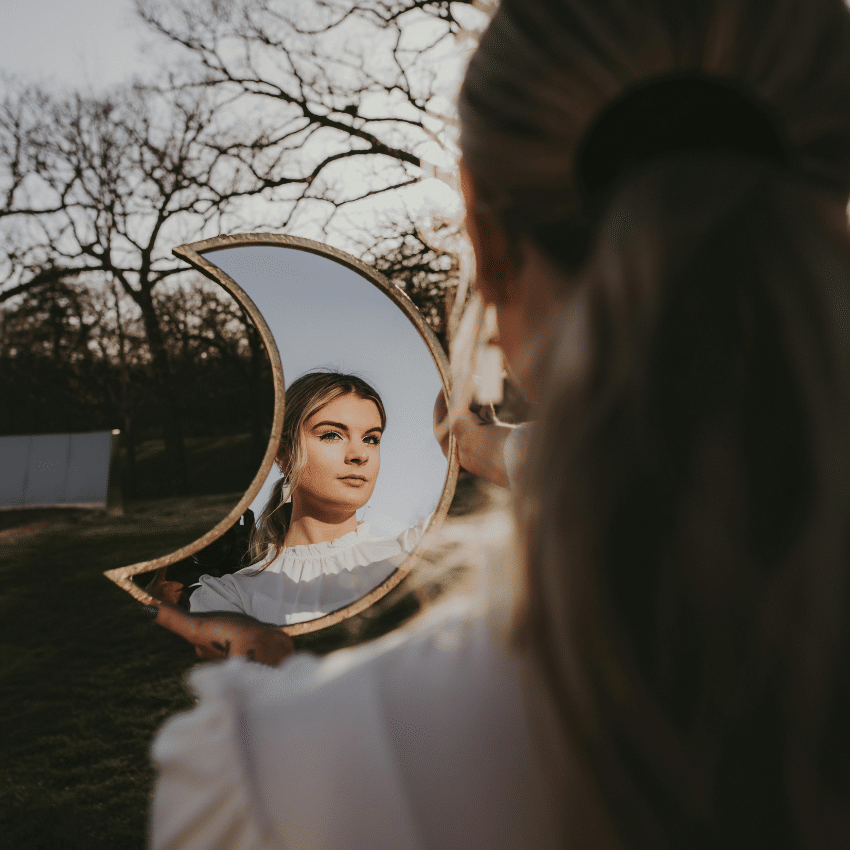 A woman looks into a crescent moon-shaped mirror, to represent the quarter moon phase occurring in this week