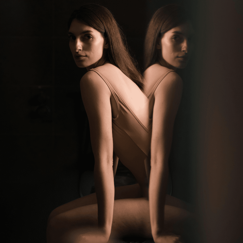 A woman sits in front of a mirror, her reflection visible to reflect the energy of this week