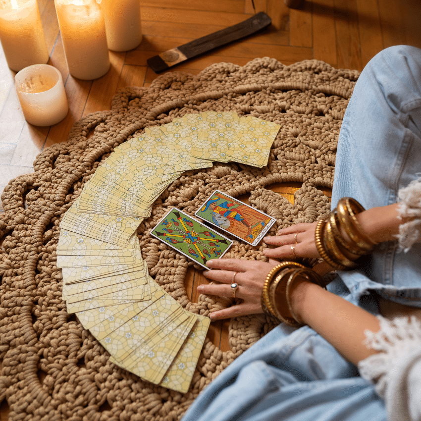 A fan of Tarot cards face down with a person sitting cross-legged in front of them. There are lit candles to represent the energy of March 2026 Tarot horoscopes.