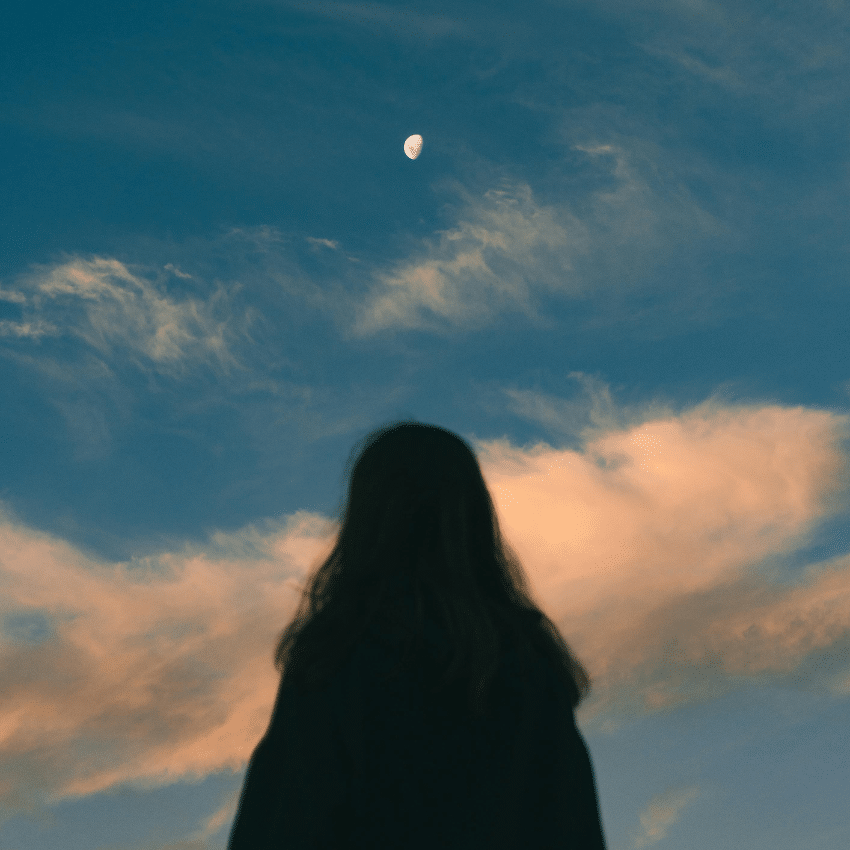 A blurred silhouette of a person looking up at the Moon in the blue sky, alluding to the sunset.