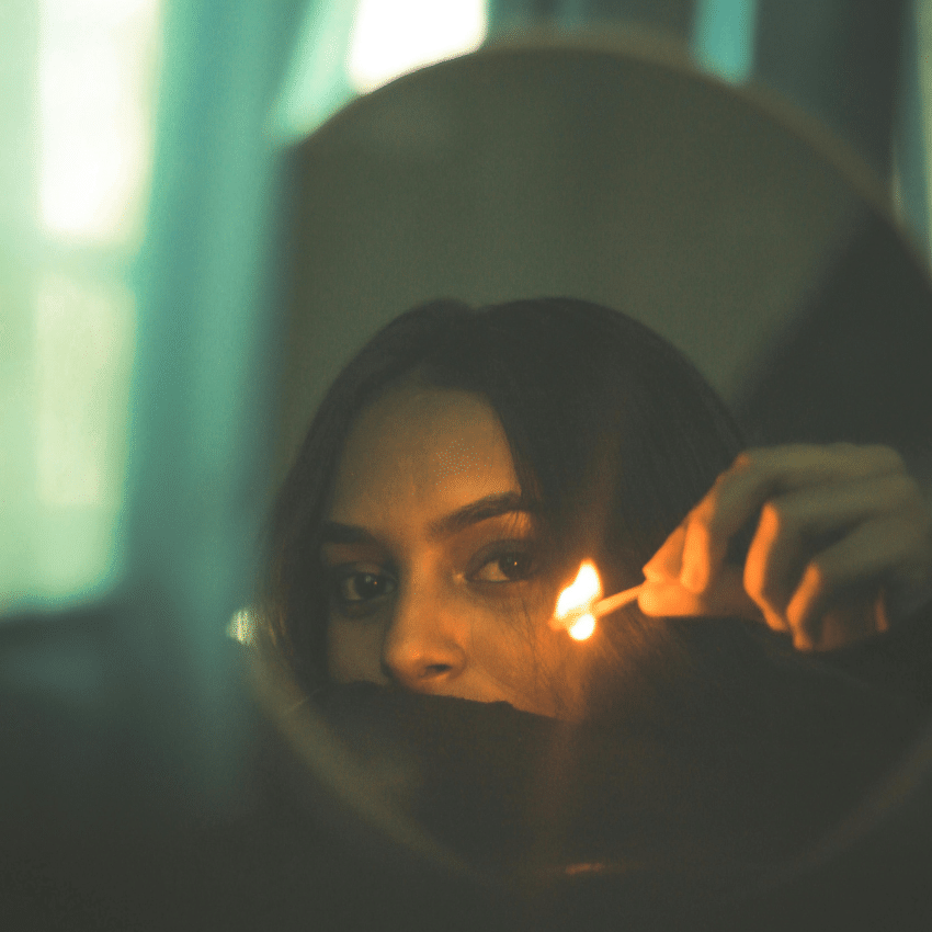 A woman holds up a lit match in a mirror, her reflection representing the energy of this week
