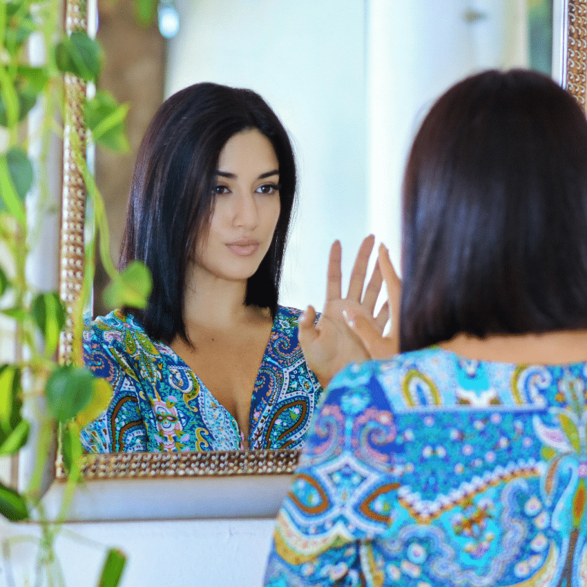 A woman looks in the mirror, touching her hand to her hand