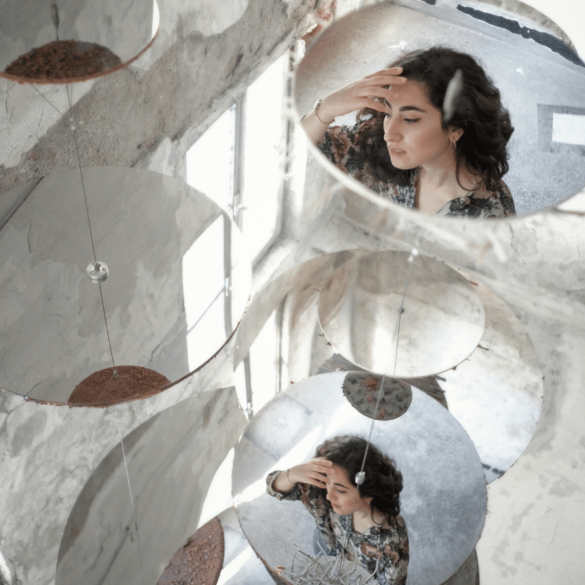 A woman's reflection in two mirrors is shown on the ground surrounded by bright light.